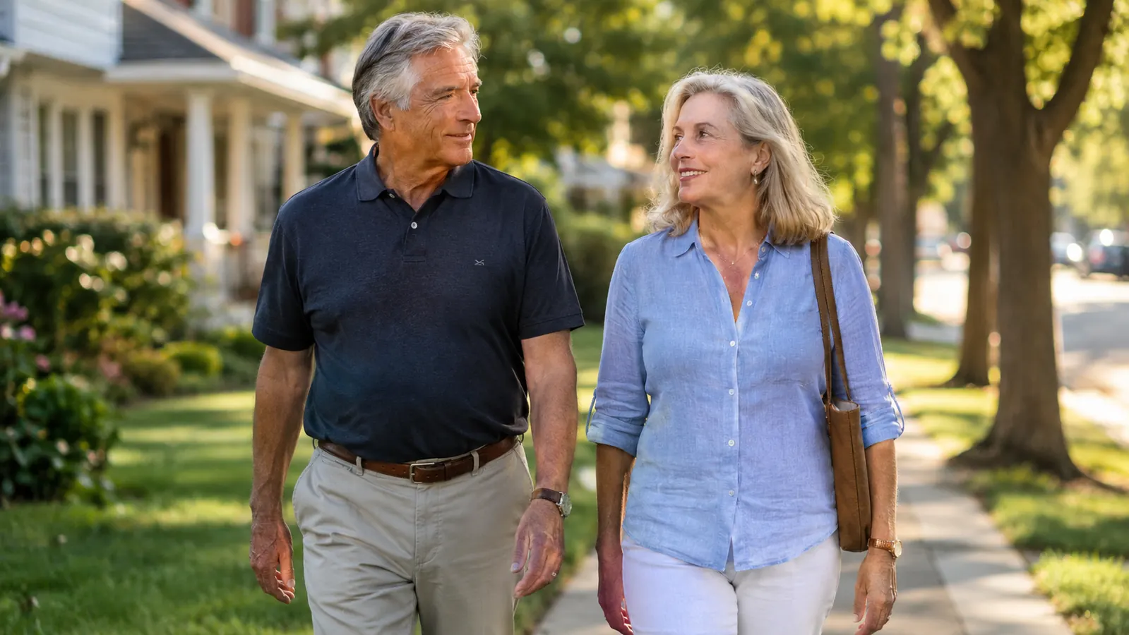 An older couple walking together on a tree-lined neighborhood street in late afternoon light